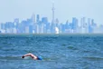 A man swims in the frigid waters of Lake Ontario overlooking The City of Toronto’s skyline in Mississauga, Ont., on Sunday, April 2, 2023. Canada's most populous city continues to endure hazy skies and poor air quality as smoke from wildfires throughout Ontario and Quebec blanket the city.