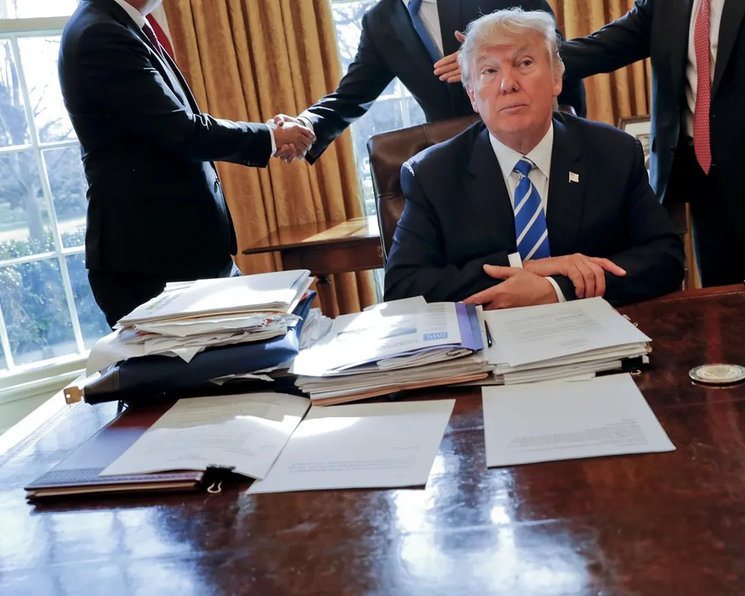 President Donald Trump sits at his desk after a meeting with Intel CEO Brian Krzanich, left, and members of his staff in the Oval Office of the White House in Washington, Feb. 8, 2017, as a lockbag is visible on the desk, the key still inside at left.
