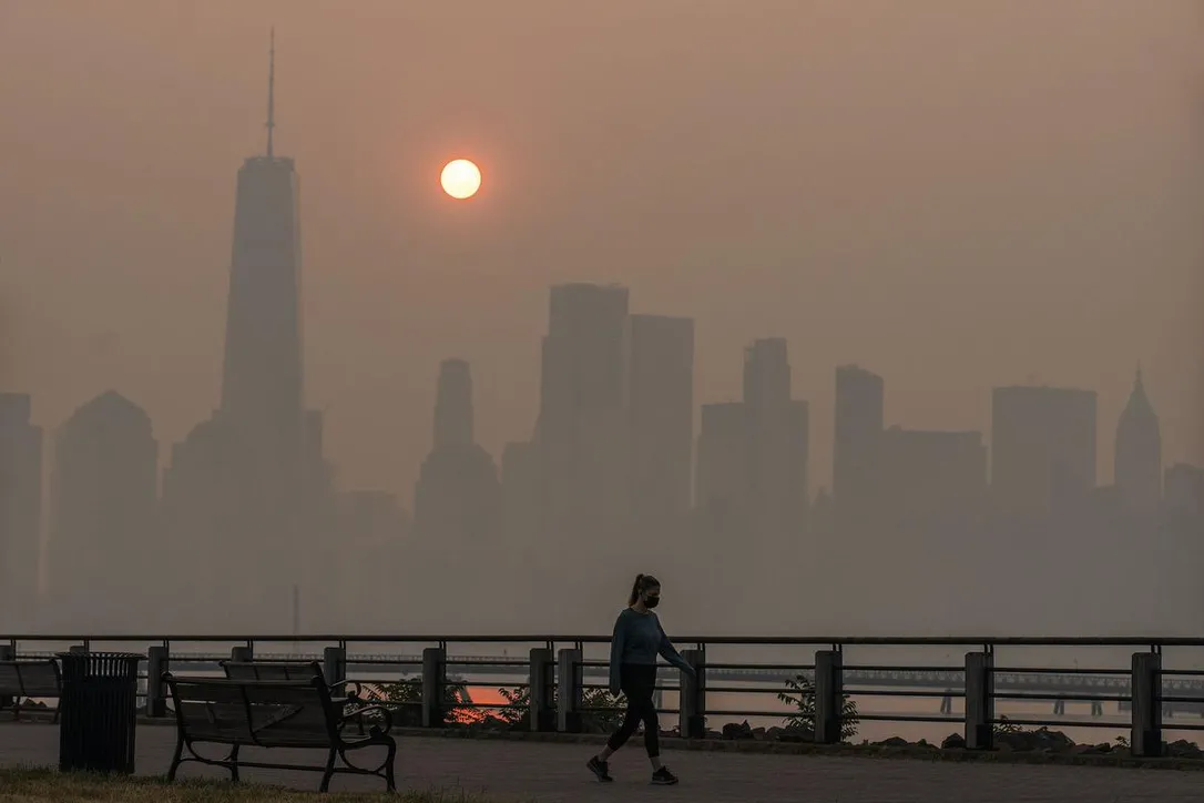 A woman walks as the sun rises behind the One World Trade Center and the New York skyline, while the smoke from Canadian wildfires covers the Manhattan borough as it is seen from the Liberty State Park on Thursday.